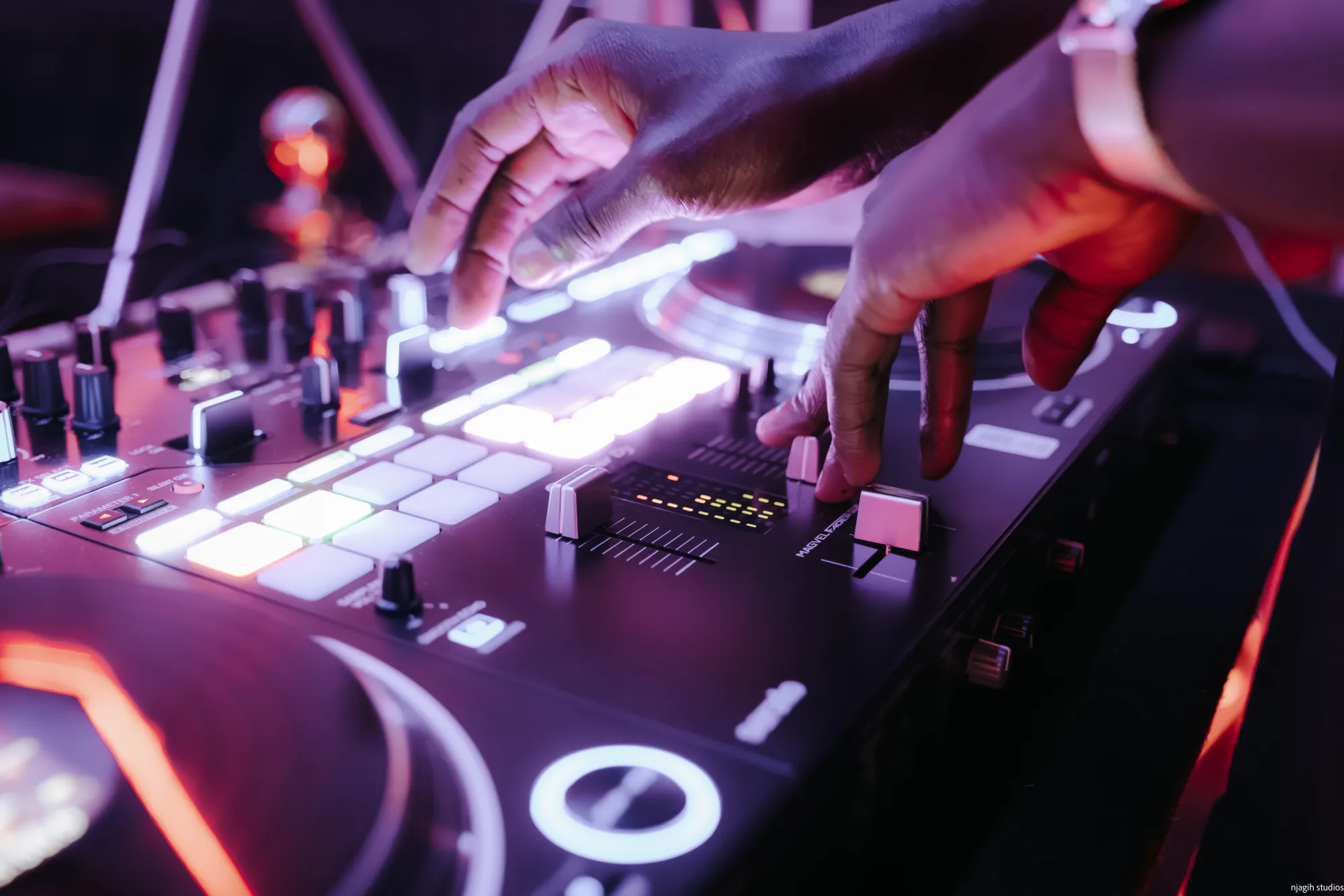DJ hands mixing on controller with glowing pads at nightclub event - Njagih Studios event photography