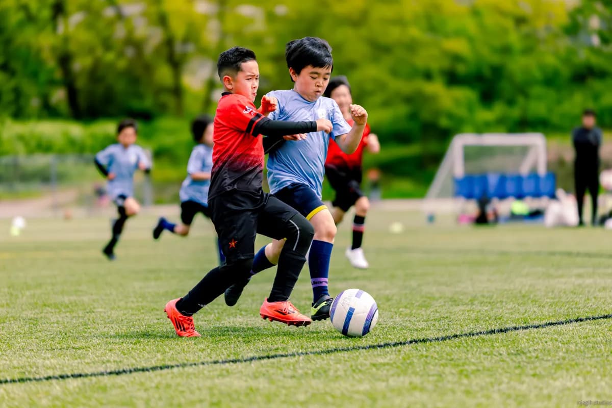 Kids competing for the ball during youth soccer match on green pitch - Njagih Studios sports photography