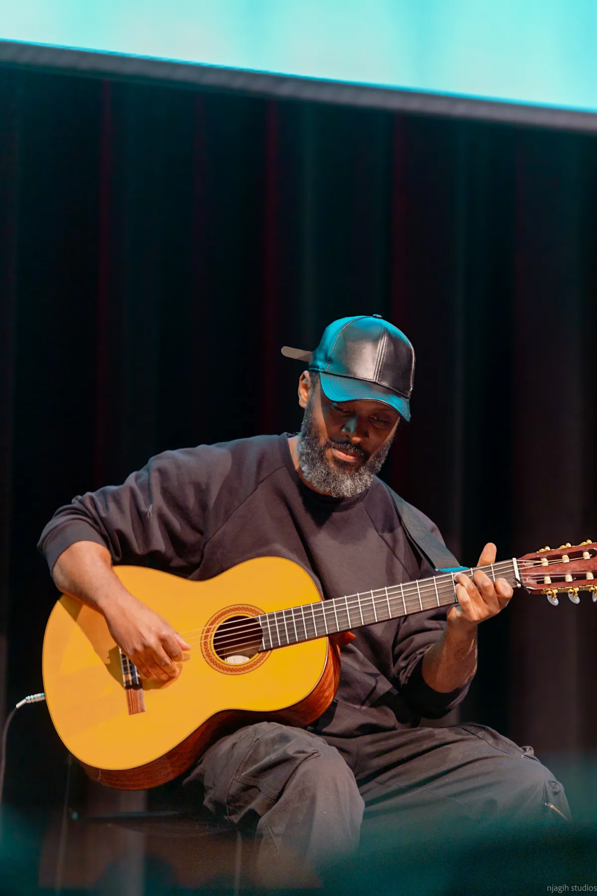 Musician playing acoustic guitar on stage at live event - Njagih Studios event photography