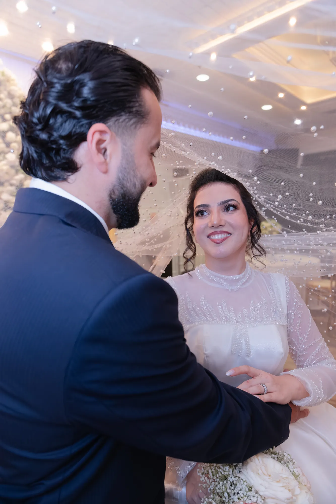 Bride and groom sharing intimate moment under pearl-beaded veil at reception - Njagih Studios wedding photography