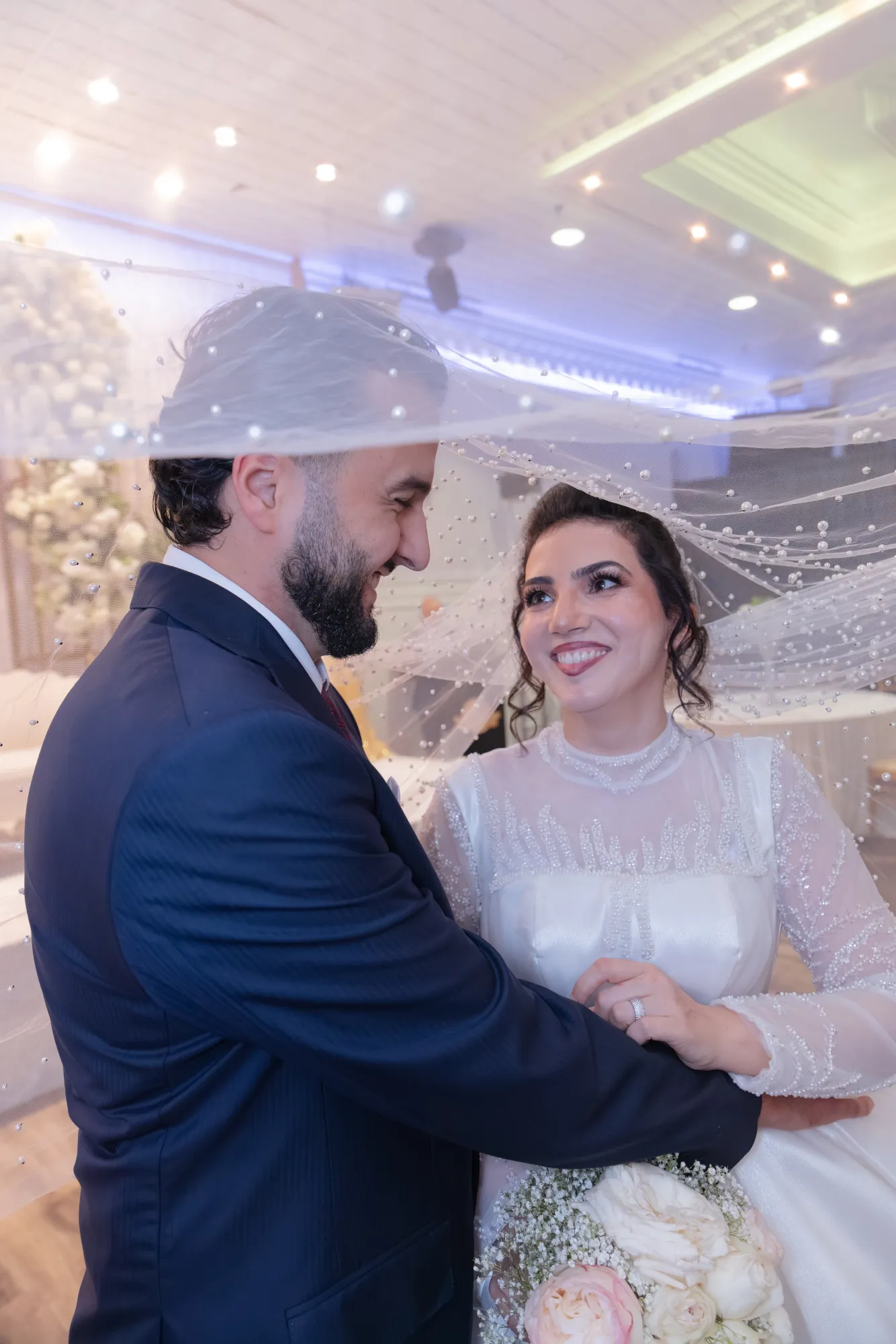 Couple embracing under pearl veil with blue reception lighting - Njagih Studios wedding photography