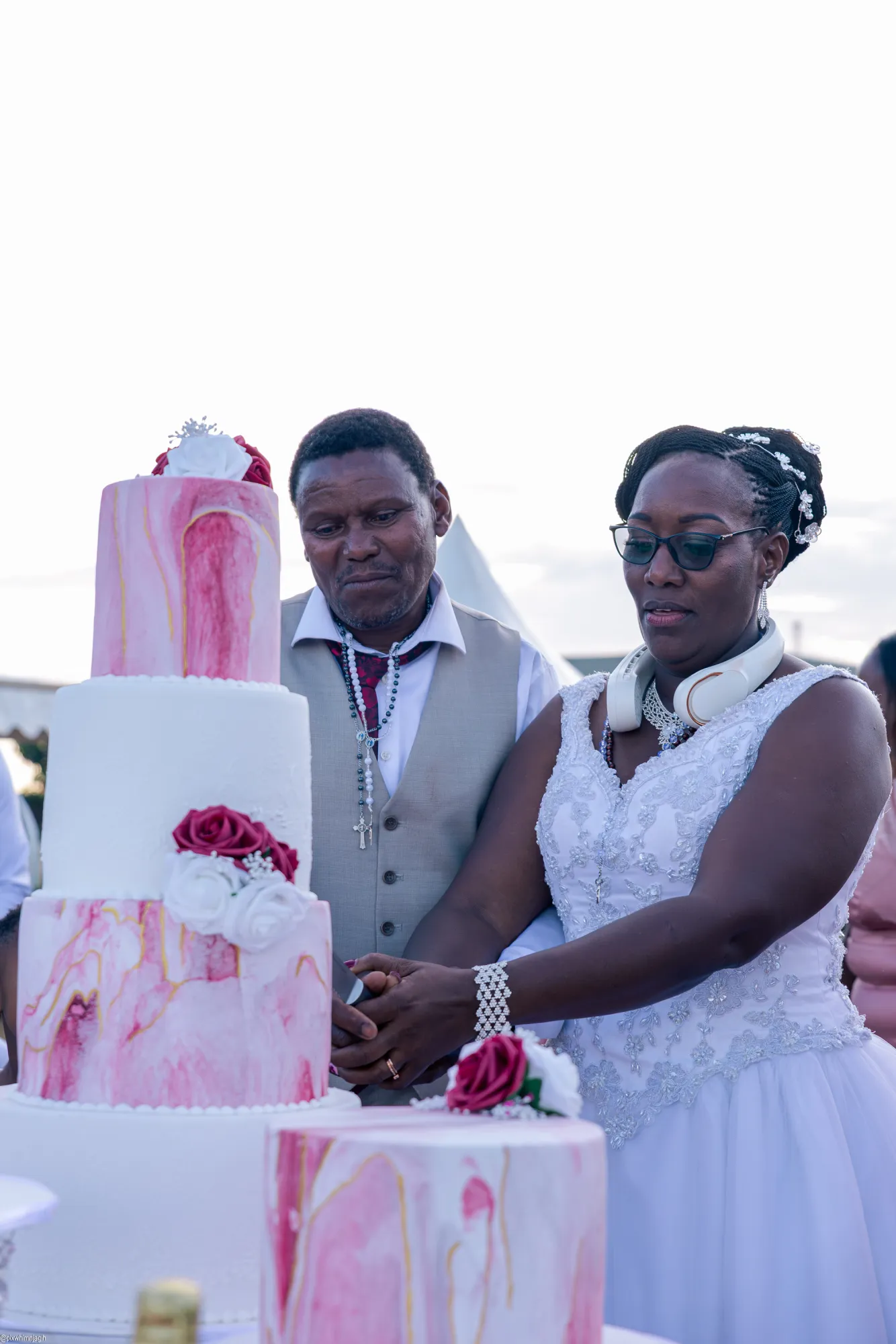 Bride and groom cutting pink marble tiered wedding cake at outdoor ceremony - Njagih Studios wedding photography