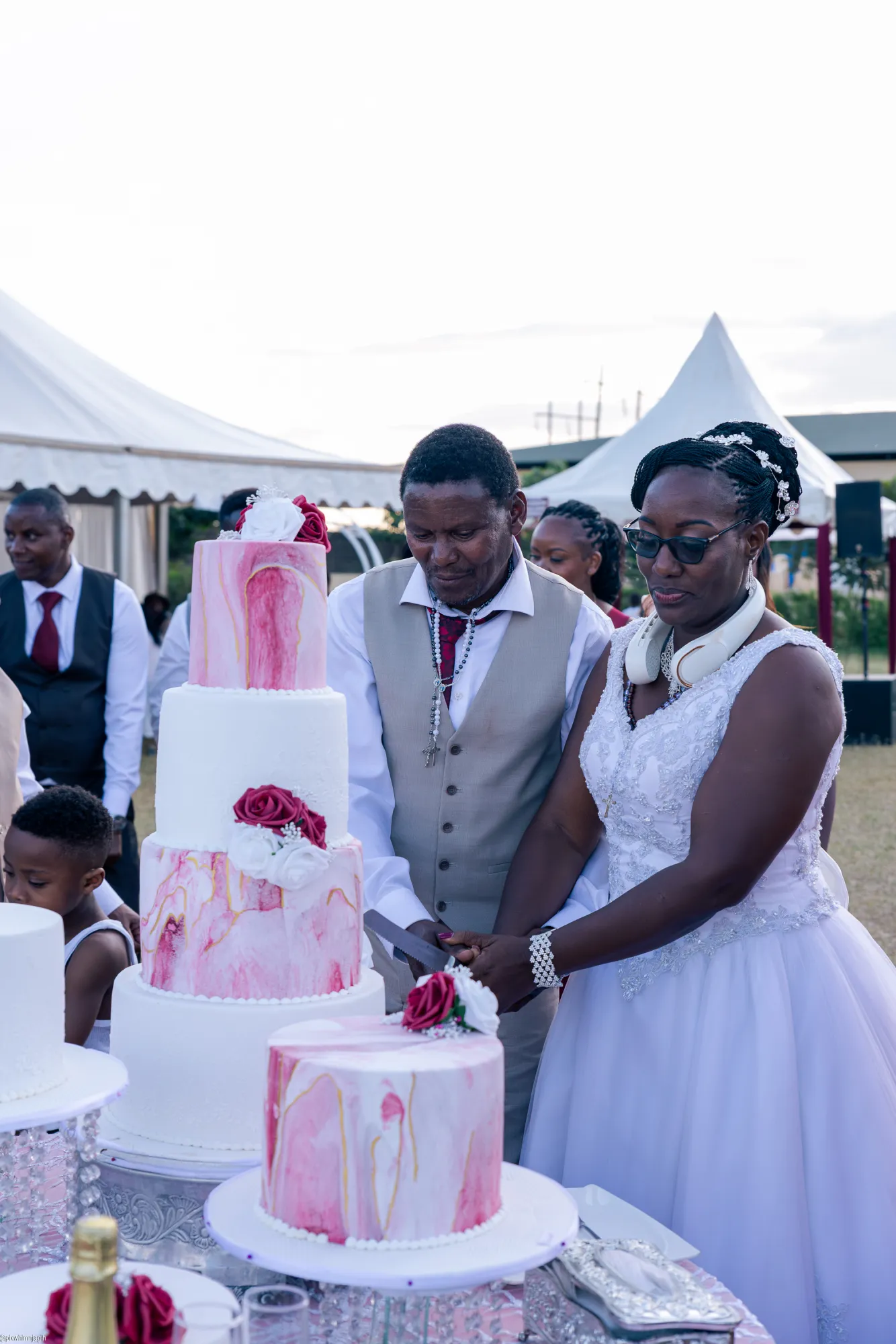 Couple cutting wedding cake at outdoor tent reception with guests - Njagih Studios wedding photography