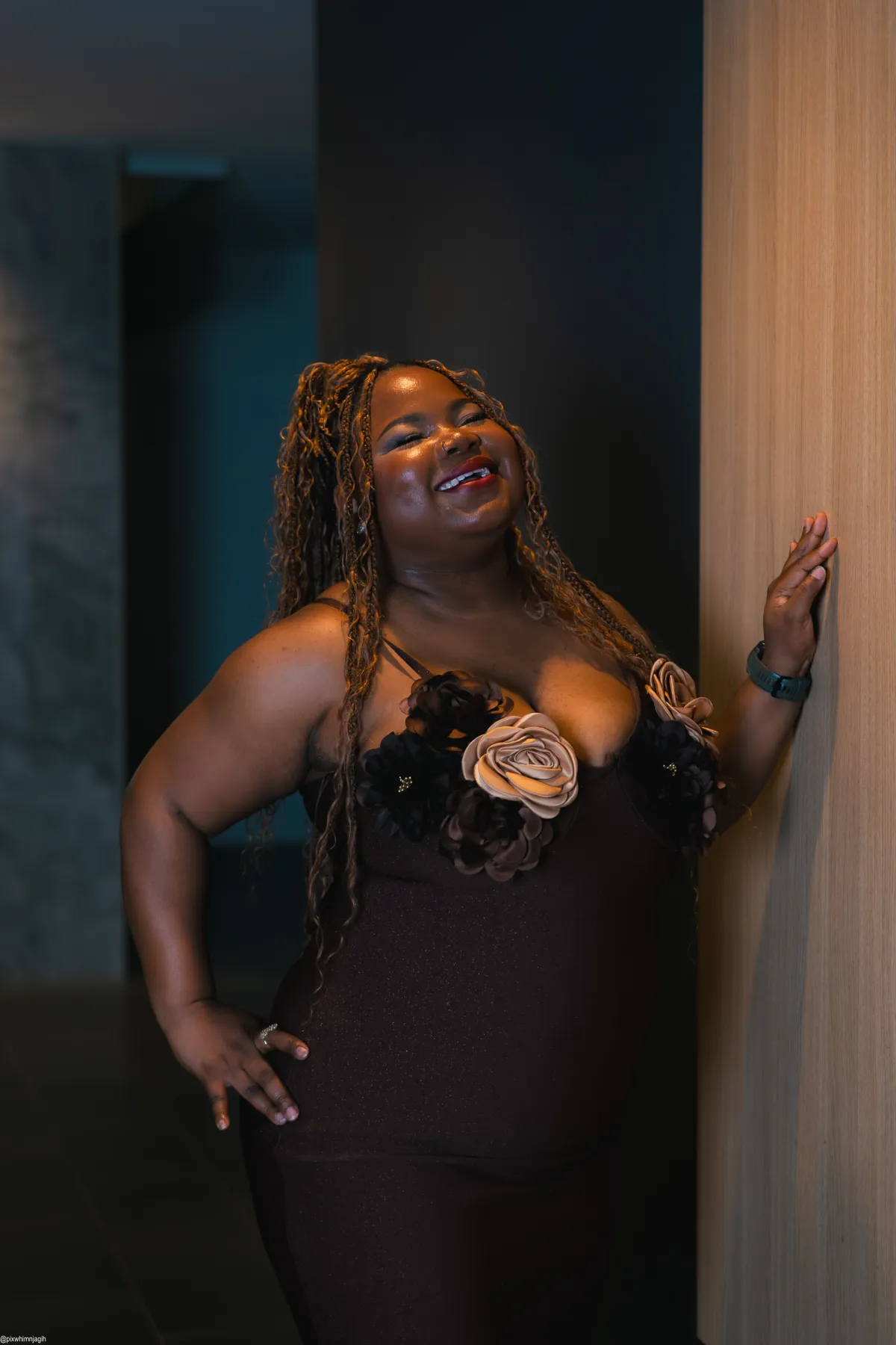 Woman in floral dress laughing against wooden wall in moody lighting - Njagih Studios portrait photography